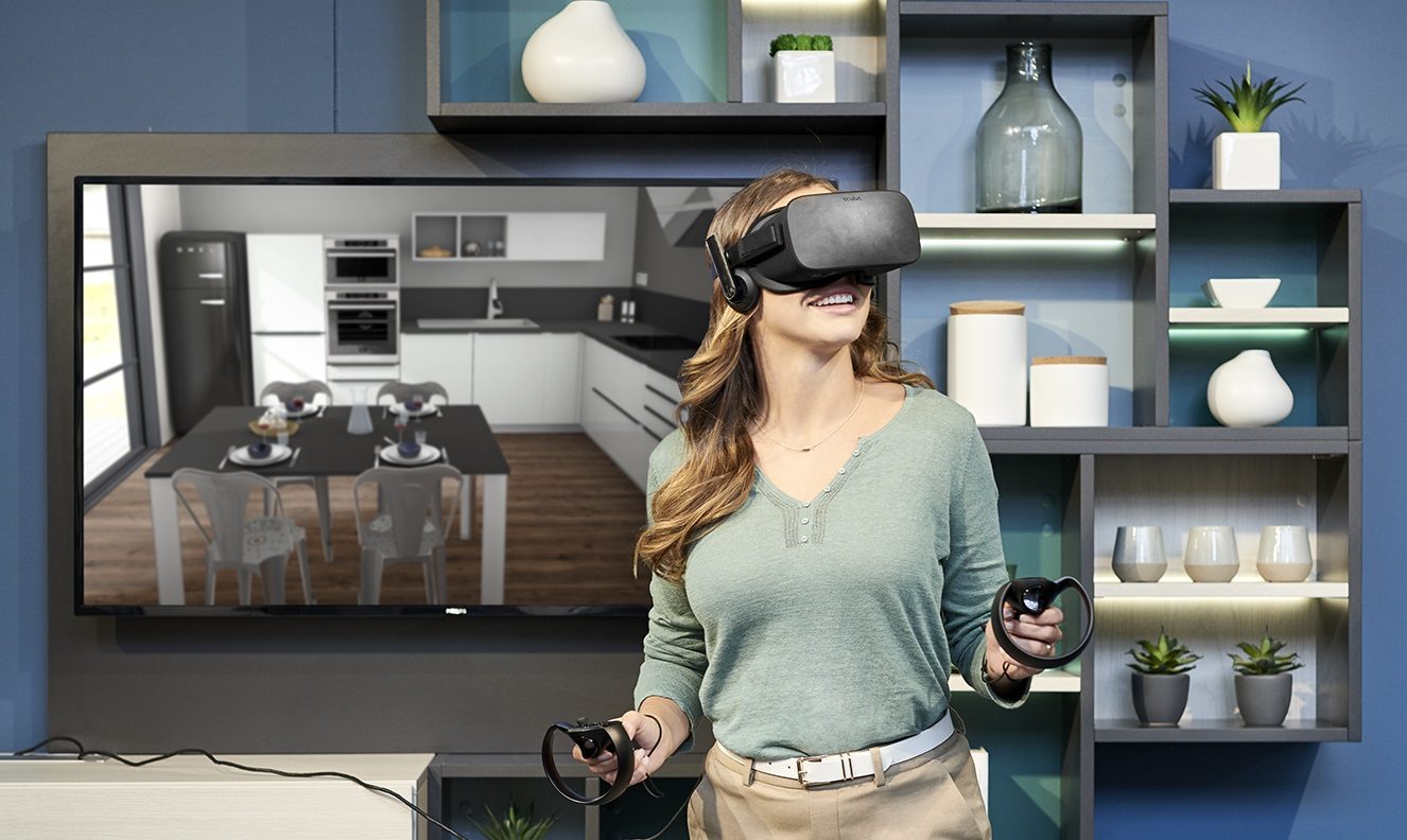 A smiling woman interacts with a VR headset in front of a kitchen visualisation on a screen. This image showcases Schmidt's use of virtual reality for kitchen design planning.
