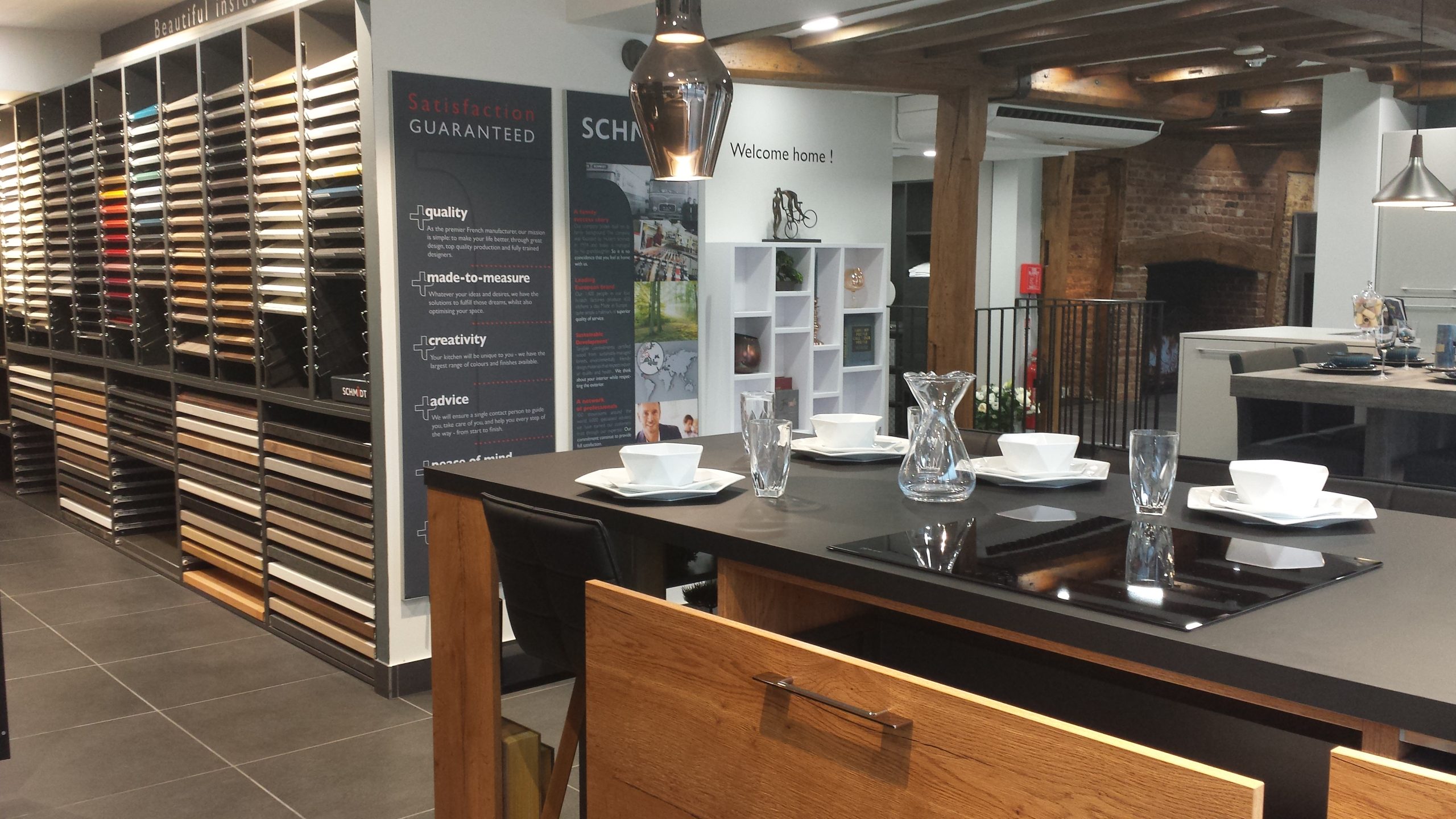 View of a Schmidt Kitchens island setup with tableware, pendant lights, and colour samples displayed.