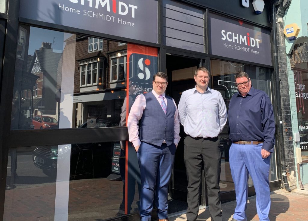 Three men in business attire stand outside a Schmidt Kitchens showroom. Captures the professional team presence and local store frontage.