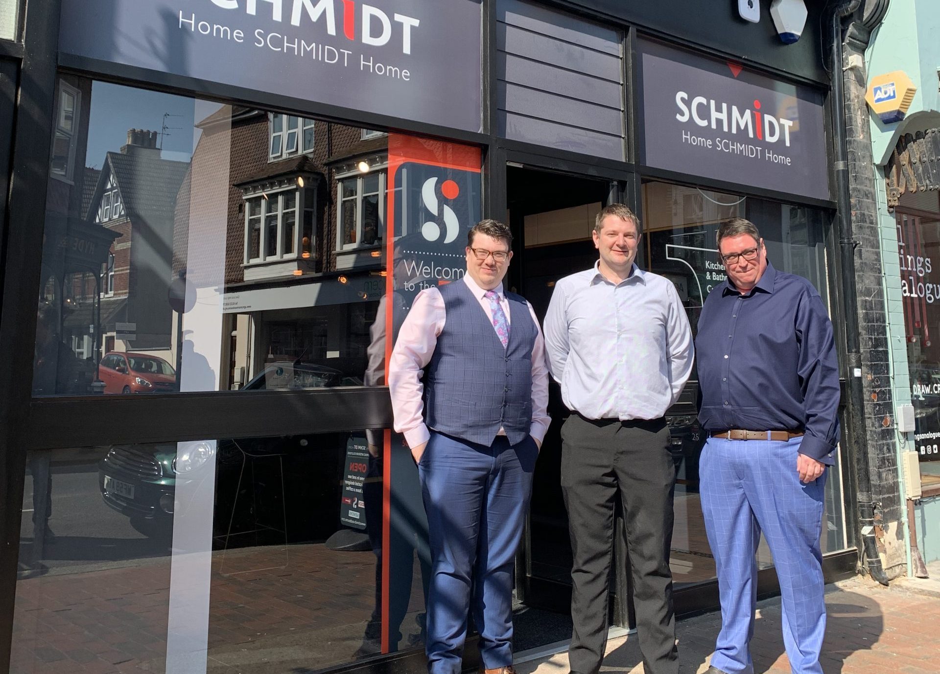 Three men in business attire stand outside a Schmidt Kitchens showroom. Captures the professional team presence and local store frontage.