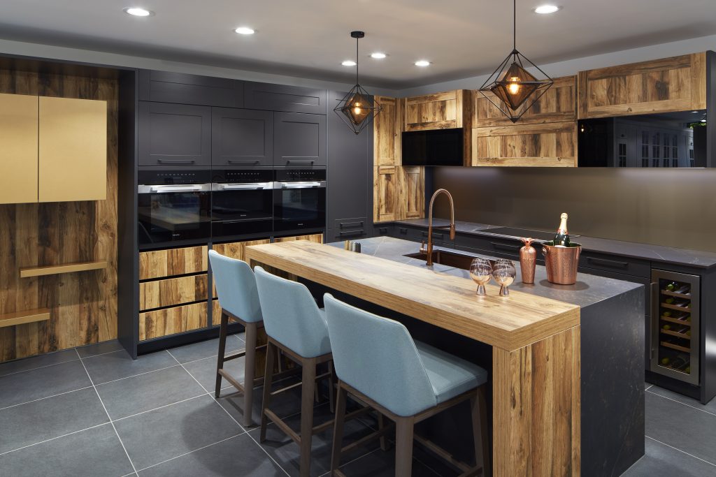 A contemporary kitchen featuring natural wood cabinetry, pendant lighting, and a spacious island with champagne glasses. The design combines rustic textures with modern appliances for a premium look.