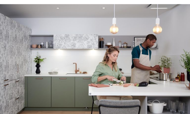 Couple cooking together in a kitchen with green and leaf-patterned cabinetry. The space blends soft colours and organic textures for a calm, modern lifestyle feel.