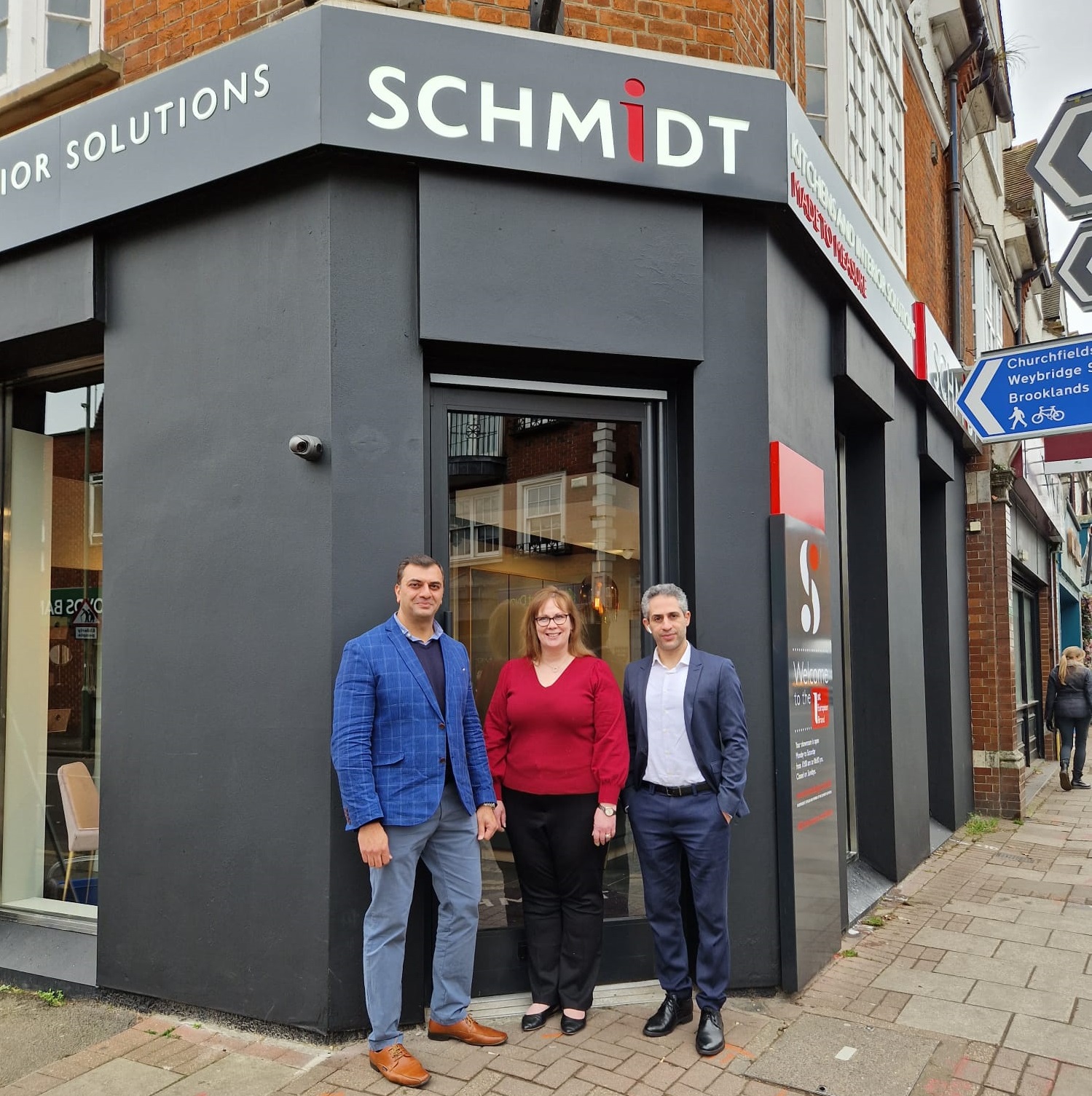 Three people stand outside a Schmidt showroom with a modern black and red exterior. The Schmidt logo is prominently displayed above the glass door.