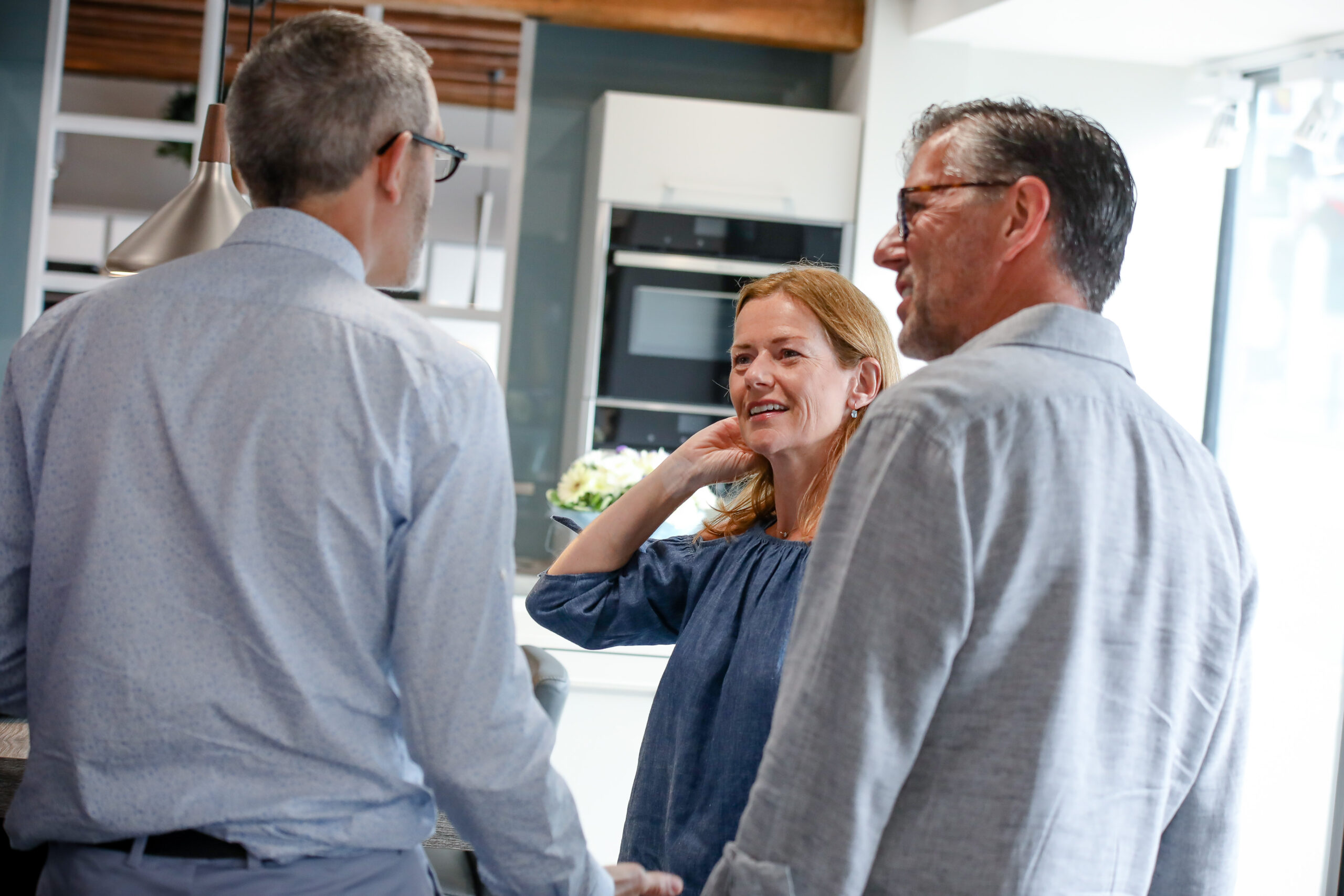 A woman and man discuss kitchen plans with a showroom consultant over sample boards. They’re surrounded by material swatches and inspiration brochures during the design consultation.