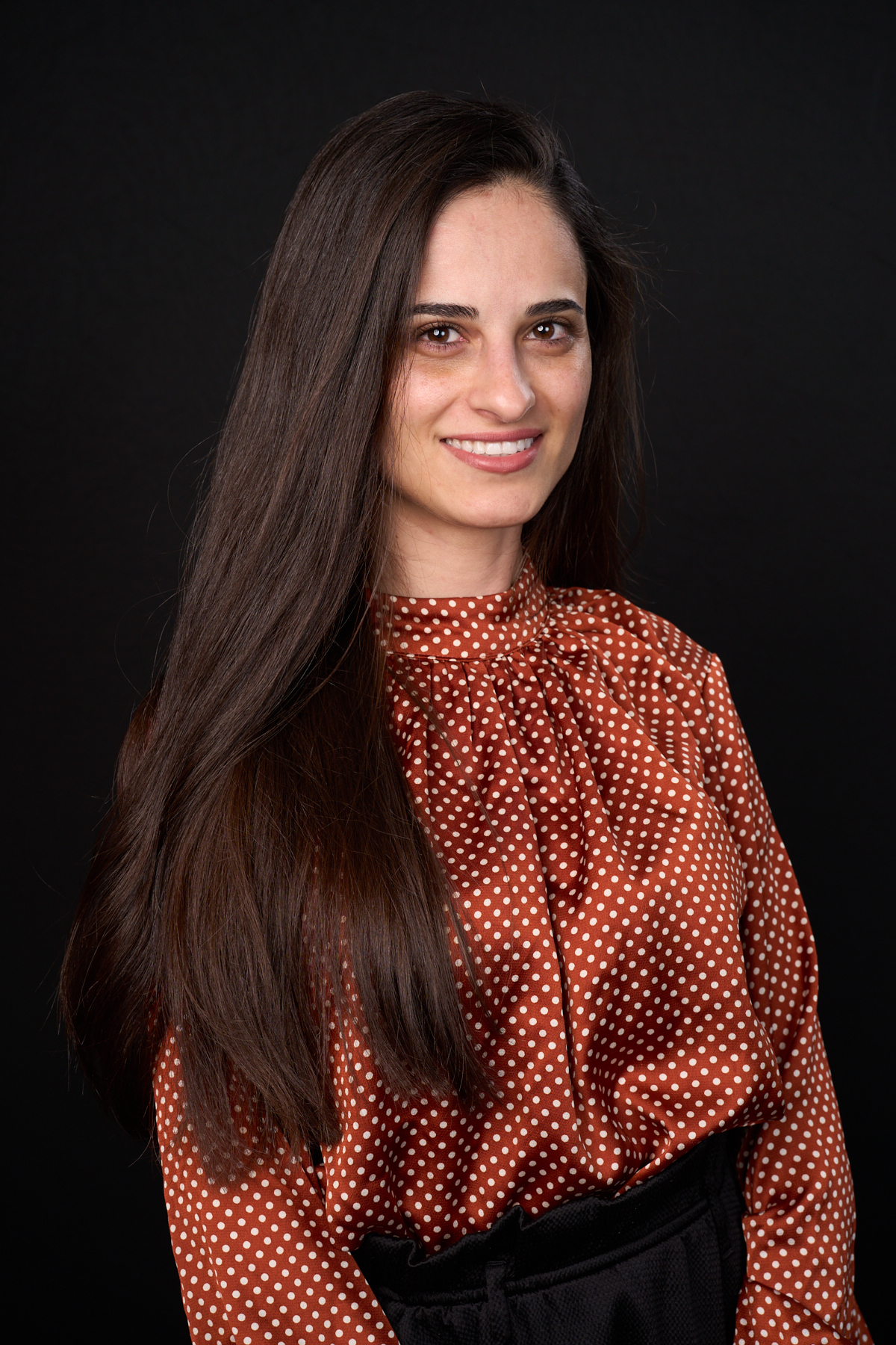 Laura Gheorghe Professional profile photo of a woman with long dark hair wearing a red and white polka dot top. A neutral black backdrop keeps focus on the subject’s friendly expression.