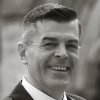 Black and white portrait of a smiling man in a suit. Professional headshot featuring a clean background and confident expression.